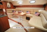 Spacious beige leather U-shaped yacht salon with a wooden table, American flag pillows, and porthole windows.