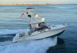 White motorboat cruising on blue water, wake trailing behind, American flag flying from the stern with a coastal town in the distance.