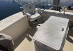 White boat cockpit with captain's chair and a large cooler/table nearby, calm water in the background.