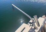 Boat deck railing extending over calm blue-green water with a sun glare on the surface.