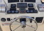 Boat cockpit helm with a stainless-steel steering wheel, gauges, and navigation controls on a beige console, ready for operation.