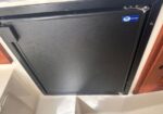 Black compact refrigerator/freezer door with a left-side handle, set in a white cabinet or boat galley.