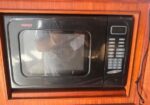 Built-in black microwave oven mounted in a wooden cabinet, with keypad and digital display on the right side.