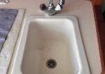 White kitchen sink with a chrome faucet on a beige counter; a towel or cloth is on the left edge of the counter.