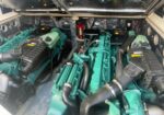 Twin green marine diesel engines in a boat's engine room, with hoses, air filters, and a red fire extinguisher visible in the background.