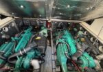 Twin green diesel engines installed in a boat's engine room, with hoses, air filters, and metal sidewalls visible between them.