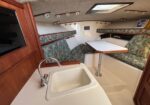 Interior of a small boat cabin: white galley sink, faucet, and a table with green patterned seating along the hull area of the cabin.