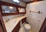 Compact boat head featuring a sink with a curved basin, wood cabinetry, and a mirror cabinet; a toilet nearby under a porthole window.
