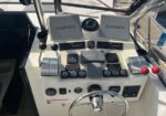 Boat helm cockpit with two Garmin displays, multiple gauges, and steering wheel; throttles on the right and red-topped controls nearby.