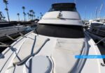 Front deck of a white luxury motor yacht with two sun loungers, anchored at a marina under a blue sky.