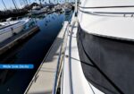 View along the wide side deck of a white yacht docked at a marina with calm water and other boats nearby, a blue label reads 'Wide Side Decks'.