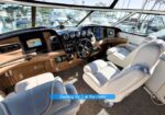 Luxurious boat cockpit with tan leather captain's chair at the helm, gauge cluster, and navigation displays, overlooking a marina.