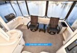 Enclosed boat lounge with two wicker chairs and a small table on a carpeted deck, large windows with a water view outside.