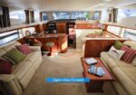 Luxurious yacht salon with cream leather seating, wooden tables and cabinetry, and large windows along the sides.