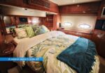 Luxurious yacht master suite with a large bed, tropical bedding, teal throw, wooden cabinets, and porthole windows.