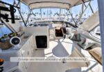 Flybridge cockpit of a white yacht with seating, helm, and large windows; marina visible outside.