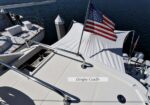 White yacht deck featuring a dinghy cradle and an American flag fluttering at a marina edge.