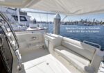 Spacious yacht cockpit with sunshade, grill, wet bar and icemaker; white seating, marina in background.