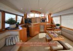 Bright yacht salon with cream leather seating, curved wood cabinetry, and a central table; large windows overlook the marina; overlay reads 'Salon is open & airy with great views all around!, view to forward...'