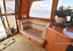Wood-paneled boat cabin with a beige leather sofa and a large window showing a marina view; a potted plant sits on a polished cabinet nearby.