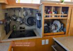 Compact kitchen with an induction cooktop, hanging pots, and an open cabinet filled with dishes.