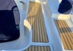 Boat deck with white fiberglass and teak-look non-slip floor panels; shaded seating area on the left.