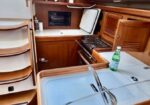 Wood-paneled boat galley with sink, two-burner stove, and storage shelves; bottled drinks on a rack.