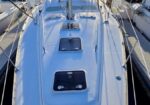 Top-down view of a white sailboat docked in a marina at sunset, with masts and neighboring boats on either side.