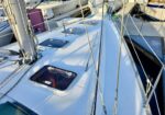 White sailboat deck at a marina, showing cabin hatches, rigging, and nearby boats.