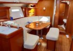 Wood-paneled sailboat interior with a beige U-shaped dinette, oval table, and two cups on the table.