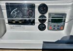 Close-up of a boat console showing gauges (fuel, tachometer, pressure), a warning label, and a small digital display panel.