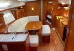 Cozy sailboat cabin with wood paneling, cream U-shaped seating around a wooden table, and warm ambient lighting.