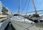 Sailboat moored at a marina with a clear blue sky and other boats nearby along a waterfront.