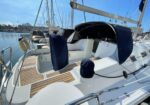 Sailing yacht's cockpit with teak deck, blue canvas covers, and an open rear hatch moored in a marina.