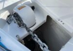 White boat anchor windlass with a heavy metal chain draped over it in the bow locker.
