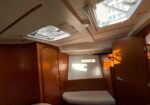 Wood-paneled sailboat cabin with a white cushioned bench seat, overhead skylights, and curved wooden cabinets.