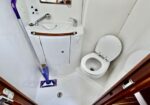 Small white compact bathroom with a toilet, sink and mirrored cabinet; a mop leaning in the corner of the tight space.