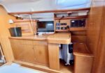 Wood-paneled yacht cabin with navigation station: chart table, monitor, radios, storage cabinets, and a small heater nearby