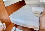 Interior of a small boat cabin with a V-berth bed, white cushions, wooden panels, and a curved stair/step area.