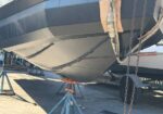 Boat hull resting on jack stands in a dry dock, with chains and straps nearby for support and maintenance access.