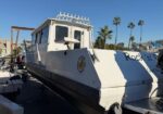 White motorboat on a trailer at a marina, logo on the hull, with a blue sky and palm trees in the background.