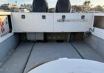 Rear of a small boat showing two raised outboard motors, white control boxes, and a view of marina houses in the background.