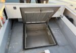 Open floor hatch on a utility truck, revealing a square recessed storage compartment with the lid raised.
