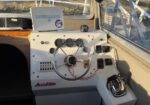 Boat helm with steering wheel, gauges, and Lowrance navigation unit; red safety lanyard visible on the console.