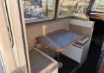 Boat cabin dinette with beige cushioned benches around a small square table with a blue marbled top, next to windowed walls.