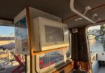 Microwave mounted on a wooden shelf inside a boat cabin; marina visible through the window.