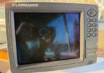 Lowrance fish finder/sonar display with keypad on the right, mounted outdoors on a boat or dock.