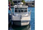 Front view of a white motorboat docked at a marina, tied to a pier with houses in the background