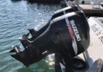 Close-up of a black Suzuki FourStroke outboard motor mounted on the back of a boat, angled over calm water.