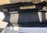 Underseat view of a car seat with black fabric covering and a warning label on the track base.